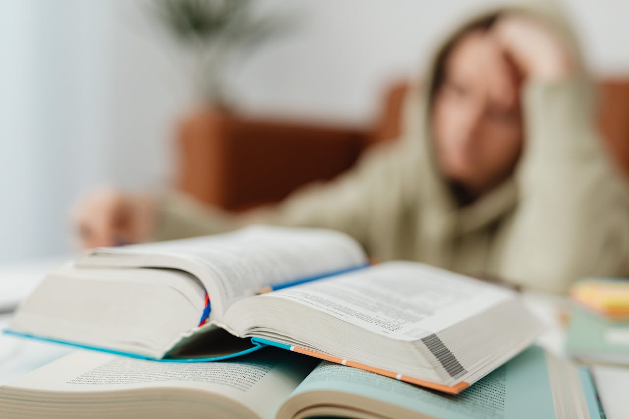 Blurred student studying at desk with open books, showcasing academic stress.