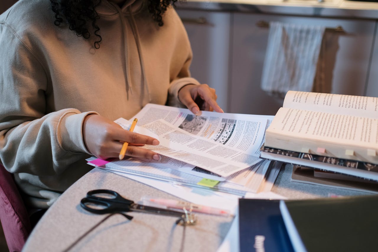 A student deeply engaged in study with books and notes spread across a table.