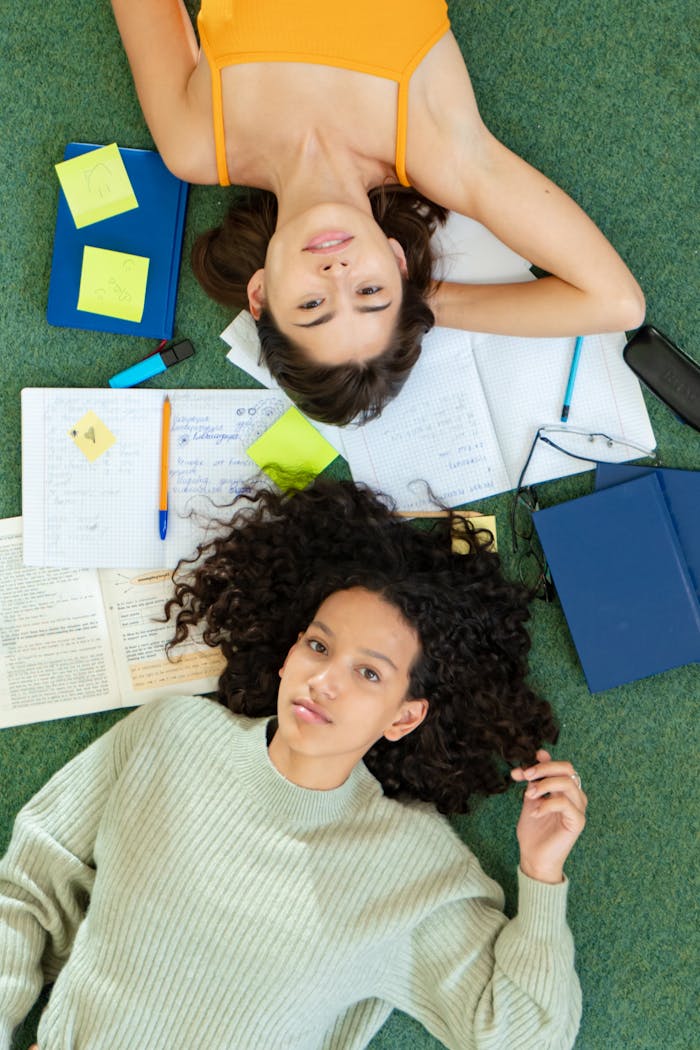 Two diverse college students lying on the floor, surrounded by study materials, showcasing creativity and collaboration.